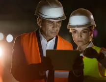 Construction professionals reviewing project information on a tablet at a worksite.